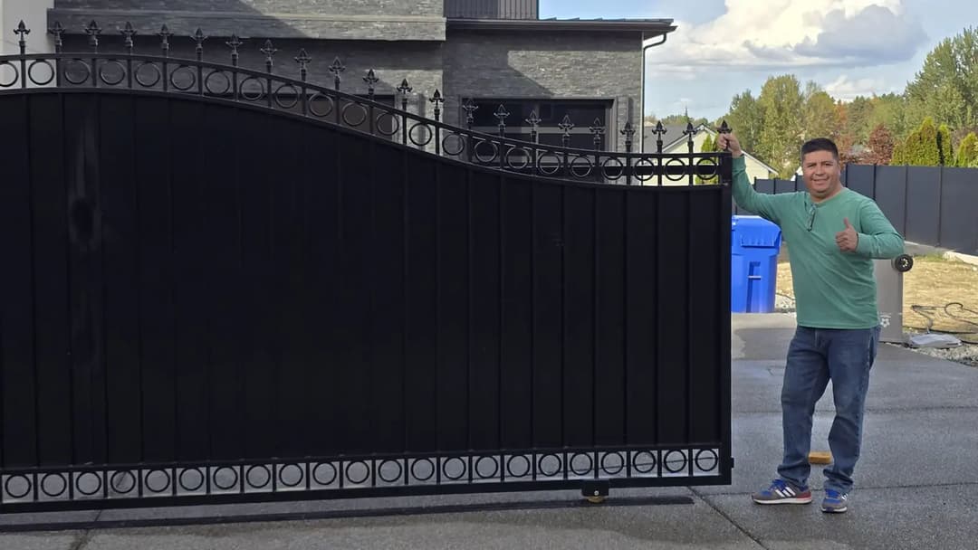Man giving a thumbs-up next to a stylish black decorative gate in a residential area.