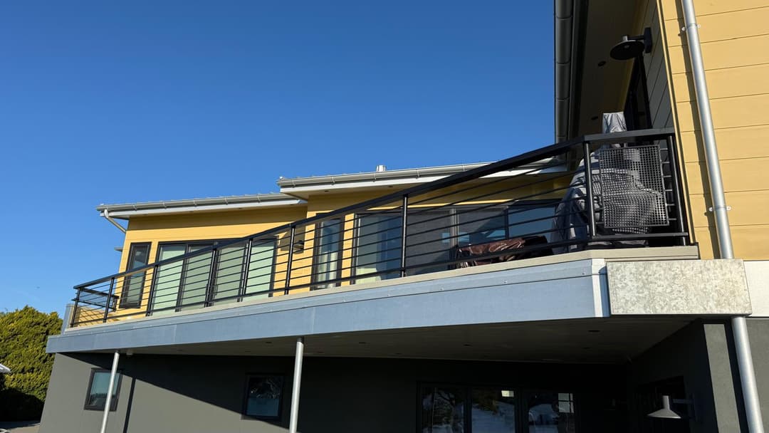 Modern yellow house with a balcony and railing under a clear blue sky.