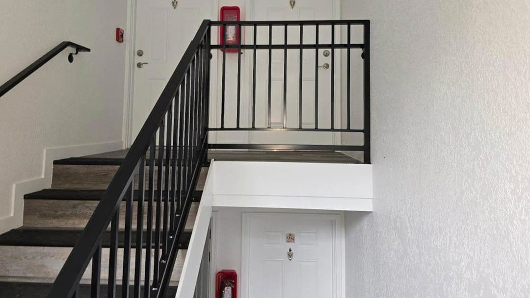 Interior stairway with black railing, leading to a white door and fire extinguisher on the wall.