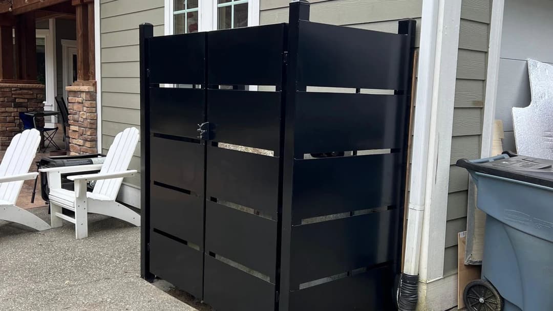 Black outdoor privacy fence with horizontal slats beside patio chairs and a trash can.