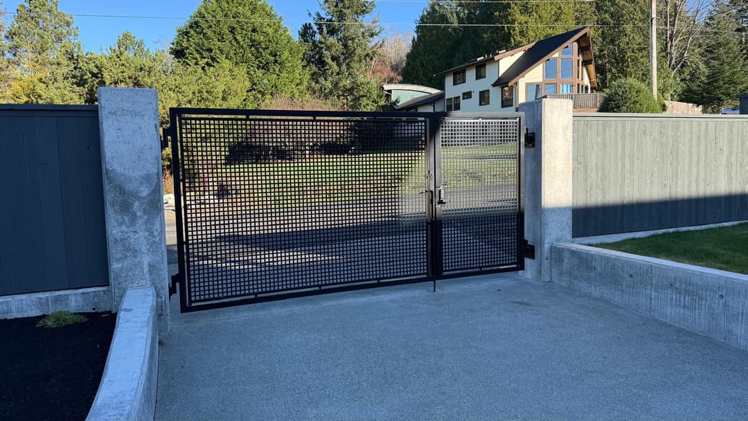 Modern black metal gate with mesh design, set in a concrete entrance against green landscape.