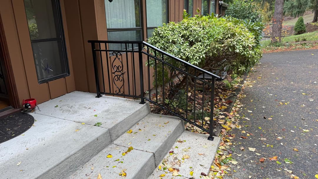 Black metal railing alongside concrete steps, surrounded by autumn leaves and greenery.