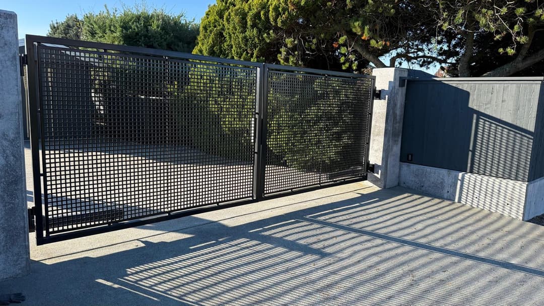 Modern black metal gate with a grid pattern, leading to a landscaped garden area.