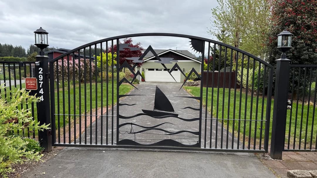 Decorative black iron gate featuring sailboat and wave design, leading to a lush green yard.