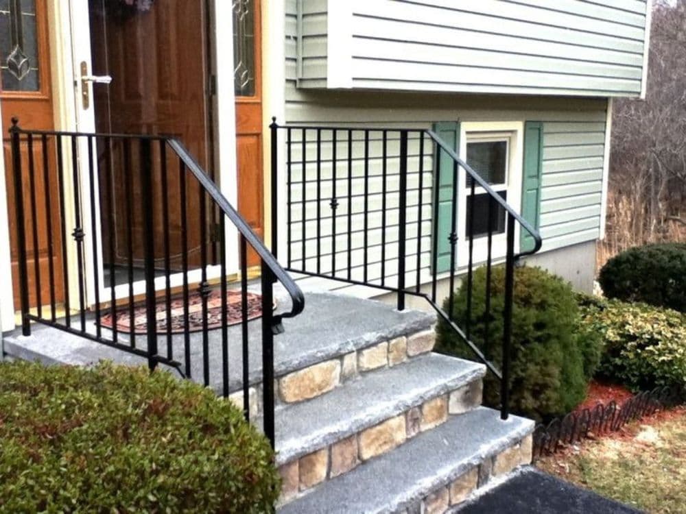 Exterior view of a home entrance with stone steps, metal railings, and well-maintained bushes.