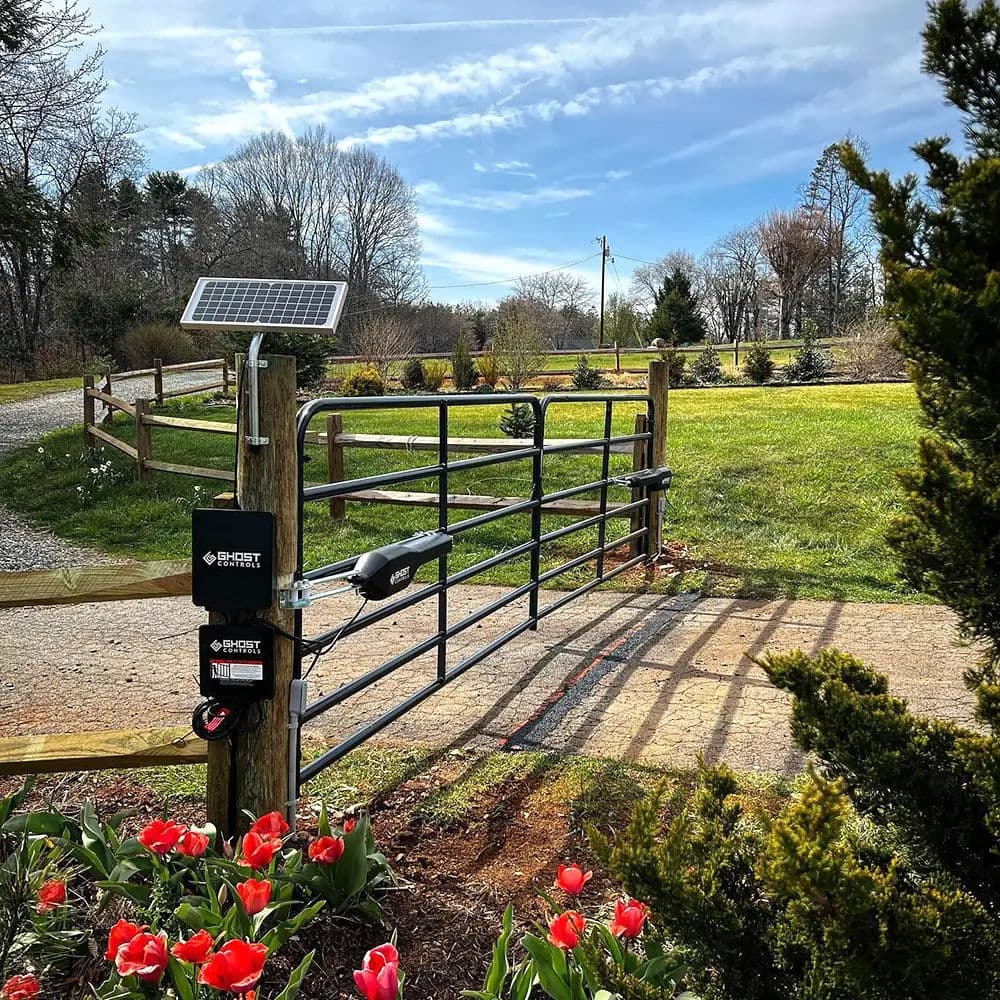 Solar-powered electric gate near a scenic pathway with blooming tulips and green landscape.