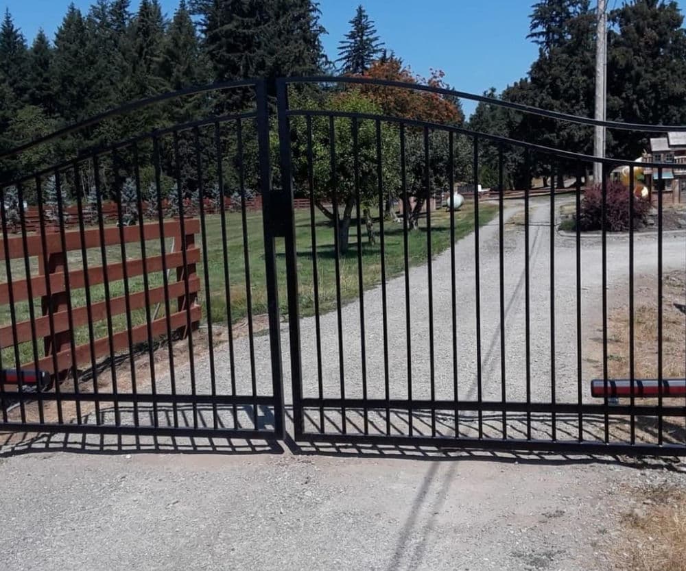 Iron gate at entrance of a gravel driveway with green trees in the background.
